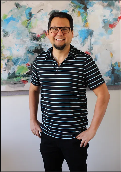 Marco Iglesias, LMFT, smiling in front of an abstract painting